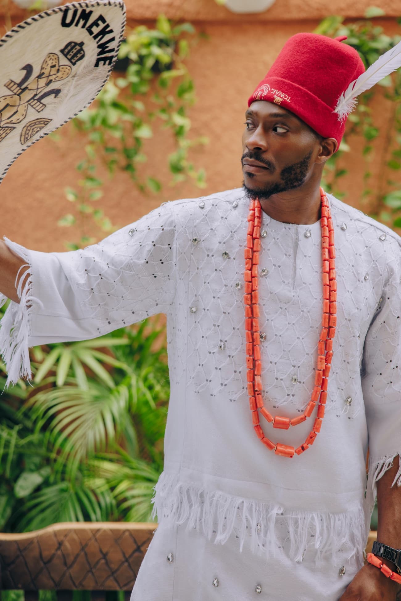 Uche Umekwe in traditional Igbo dress, holding a fan bearing the family name Umekwe.